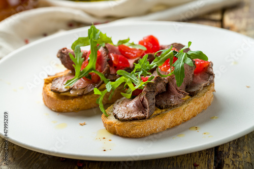 Bruschetta with roast beef, tomatoes and aragula on white plate