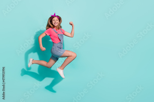 Full length profile side photo of kid girl jump go hurry discount wear striped t-shirt shorts isolated on cyan color background