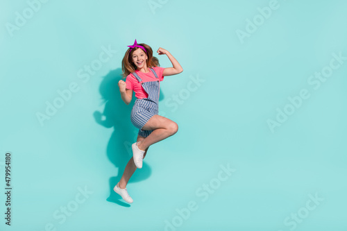 Fototapeta Naklejka Na Ścianę i Meble -  Full size photo of kid girl jump fists up win contest wear t-shirt trendy stylish isolated turquoise color background