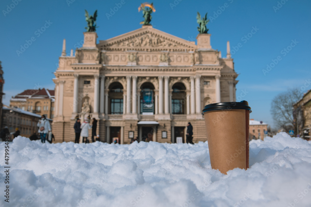 disposable coffee cup in snow lviv city opera building on background