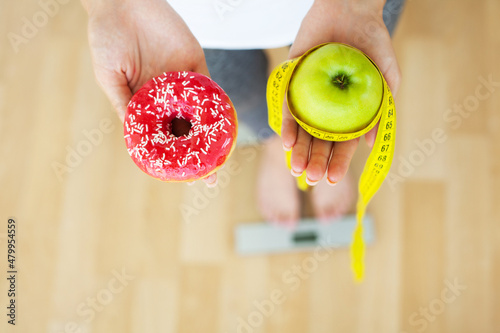 Women is choosing choice between donut and green apple during her dieting session.