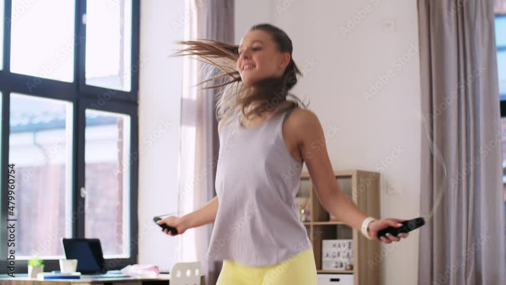 fitness, sport and healthy lifestyle concept - happy smiling teenage girl skipping with jump rope at home fitness, sport and healthy lifestyle concept - happy smiling teenage girl skipping with jump rope at home