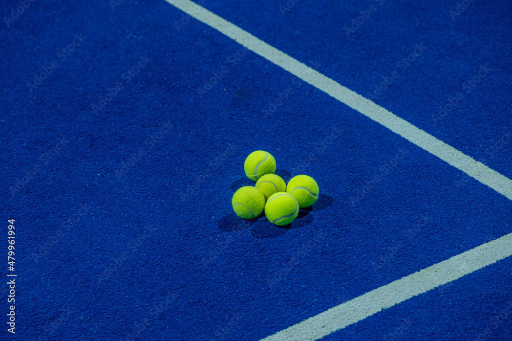 Five paddle tennis balls on the artificial grass surface of a blue paddle tennis court.