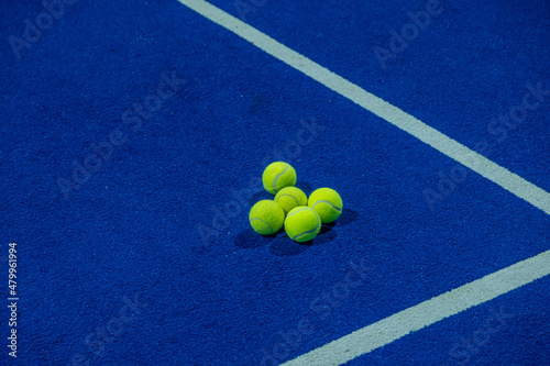 Five paddle tennis balls on the artificial grass surface of a blue paddle tennis court. © Vic