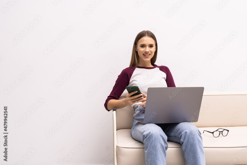 Smiling young woman using mobile phone while sitting on a couch at home with laptop Smiling young woman using mobile phone while sitting on a couch at home with laptop