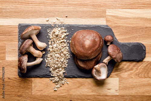 Flat lay view of dry powder made of shiitake mushrooms, Lentinula edodes. Food ingredient on black stone cutting board with fresh shiitake mushrooms. Copy space. photo