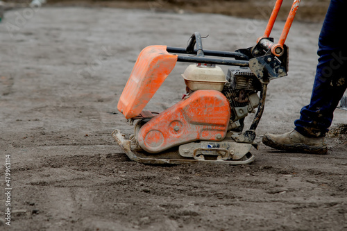 Construction worker using petrol powered plate compactor to compact stone during footpath construction on new residential development construction site photo