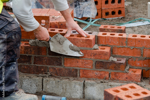 Bricklayer laying bricks on mortar on new residential house construction