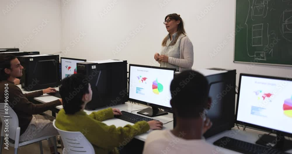 Mature teacher working with students inside computer classroom at school Mature teacher working with students inside computer classroom at school