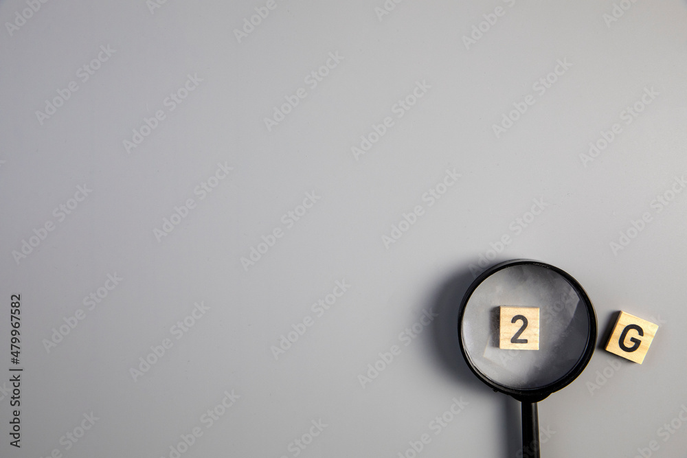 Fototapeta premium 2G on gray background with magnifying glass for covi-19, ccoronavirus, pandemic rules concept top view copy space