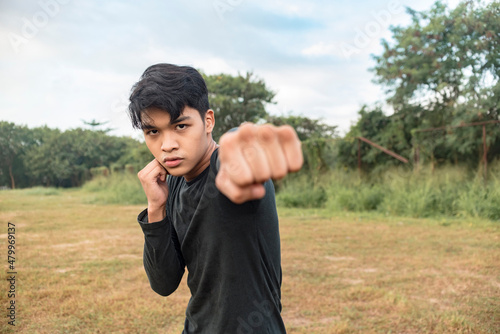 Quadro su tela A serious young man in a dark gray sweatshirt doing shadow boxing outside a field