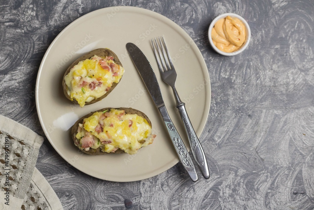 Potatoes with cheese filling and sauce in a bowl on a plate with a fork and a knife on a gray background Potatoes with cheese filling and sauce in a bowl on a plate with a fork and a knife on a gray background