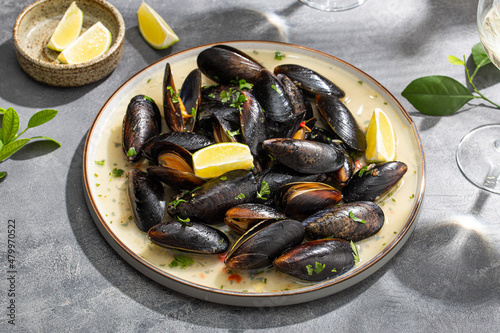 Black mussels in garlic sauce with herbs and lime and two glasses of white wine on the table under the summer sun