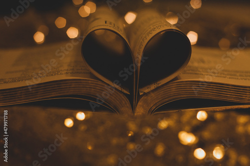 Heart shaped book pages on shiny golden bokeh background