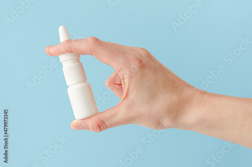 Female hand holding nasal spray on blue background. Seasonal allergy and common cold concept.
