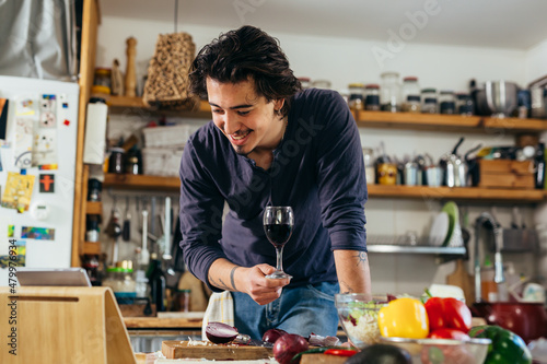 man preparing vegetable salad at home while drinking red wine