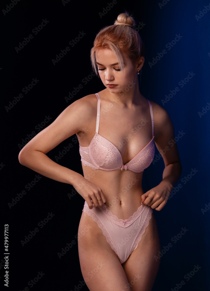 Gorgeous woman posing in seductive pink lingerie. Attractive seduce beauty lady. Advertising underwear sensual slim fit body on dark blue background free space for text Gorgeous woman posing in seductive pink lingerie. Attractive seduce beauty lady. Advertising underwear sensual slim fit body on dark blue background free space for text