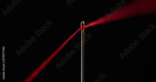 Red thread going through needle eye, closeup photo