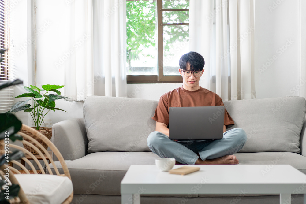 Technology Concept The male who is wearing casual clothes sitting on the sofa, resting his notebook on his lap and doing his work Technology Concept The male who is wearing casual clothes sitting on the sofa, resting his notebook on his lap and doing his work