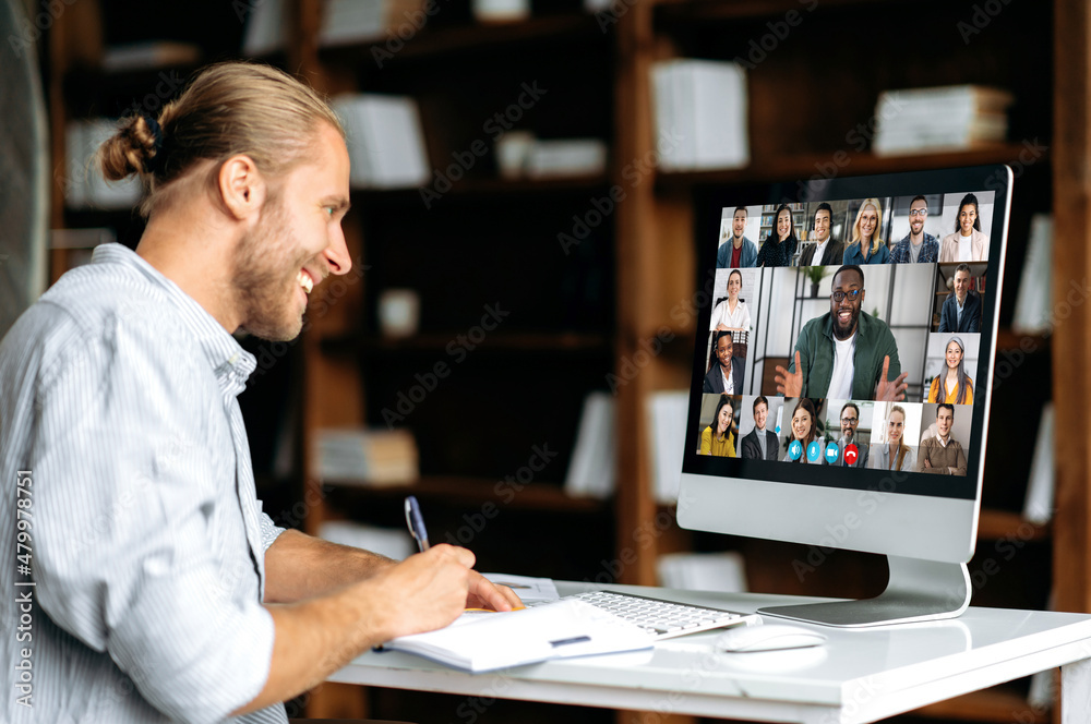 Smart modern Caucasian guy, student or freelancer, listens to an online webinar, lecture, notes information, studies remotely via video conference. E-learning concept