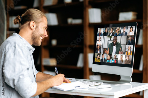 Smart modern Caucasian guy, student or freelancer, listens to an online webinar, lecture, notes information, studies remotely via video conference. E-learning concept