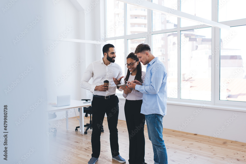 Fototapeta premium Group of cheerful male and female colleagues in smart casual wear discussing web content on financial website using modern cellphone and touch pad technology in office interior, business lifestyle