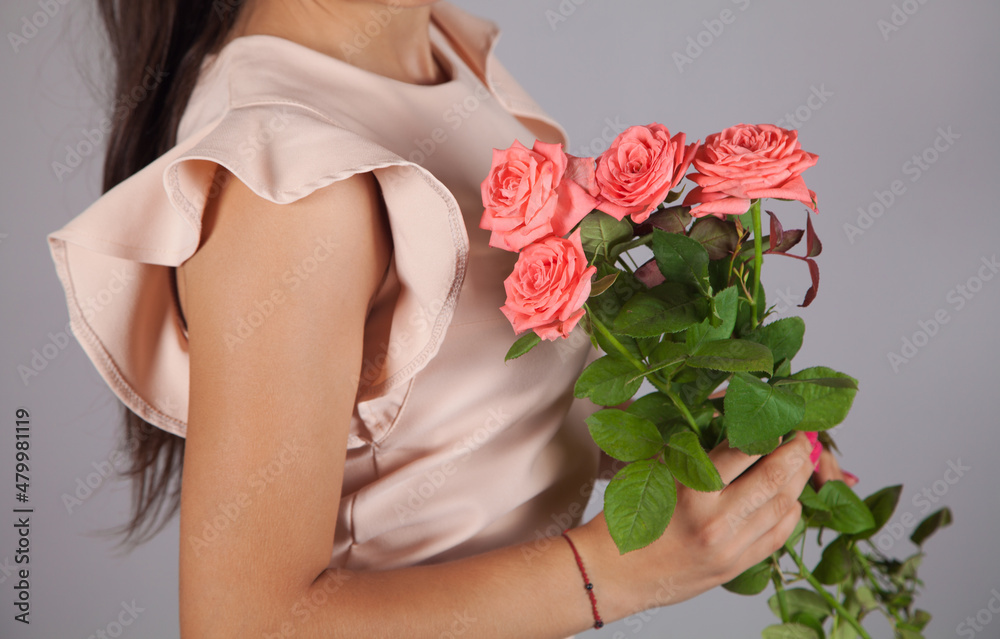 Young woman holding roses bouquet, gray color background.