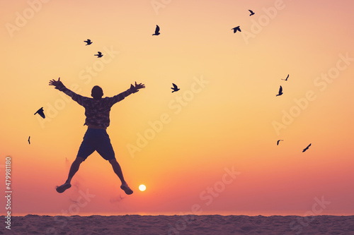 Happy man jumping at tropical beach with birds flying on sunset sky abstract background.