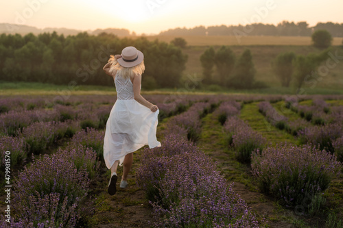 Beautiful young healthy woman with a white dress running joyfully through a lavender field, straw hat