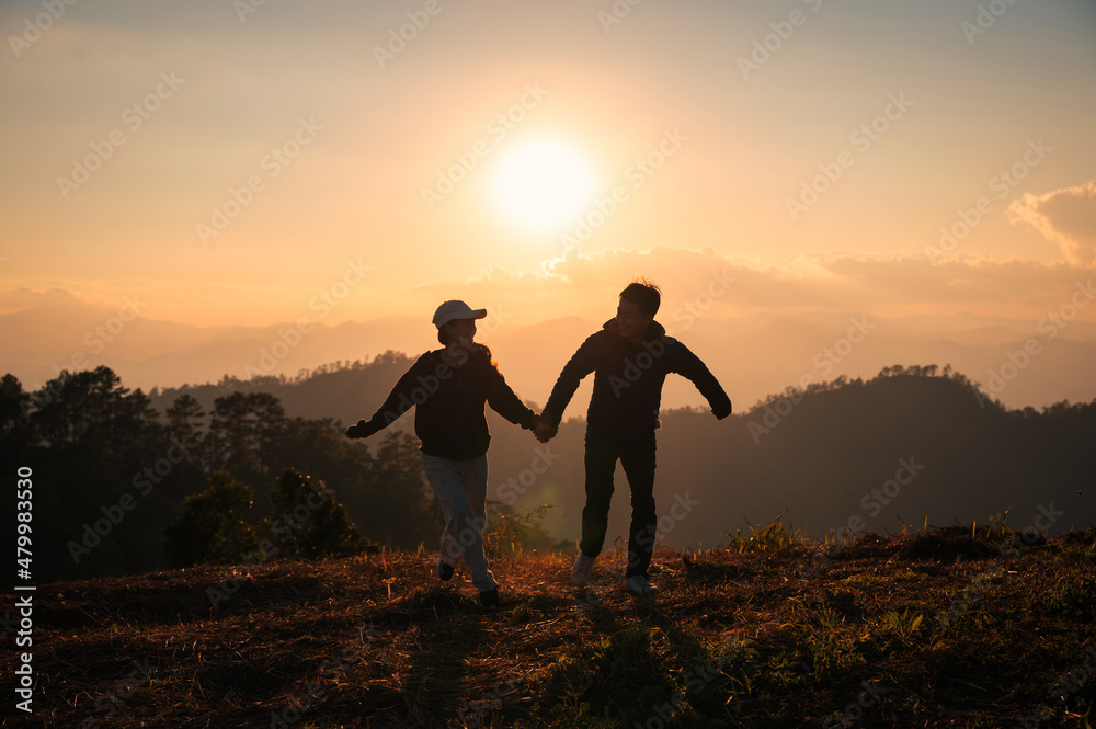 Young asian couple holding hands enjoying on hill in countryside at sunset