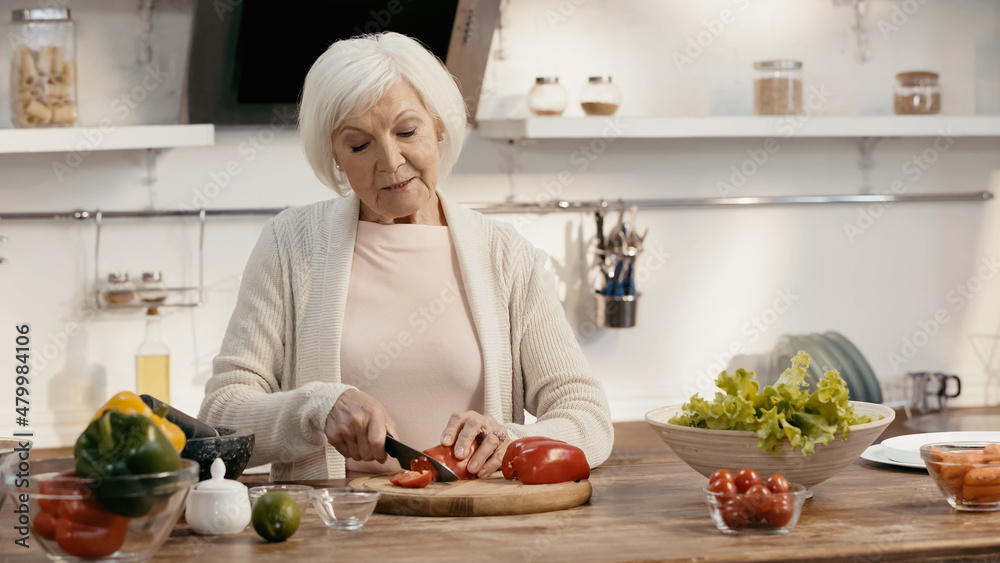 senior woman cutting bell pepper near fresh vegetables on kitchen table. senior woman cutting bell pepper near fresh vegetables on kitchen table.