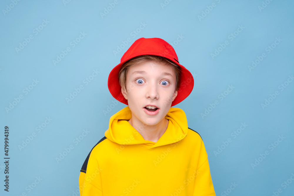 Portrait surprised young guy in yellow sweater and red panama hat on a blue background, looking at the camera with a smile on his face. Caucasian teenager posing in studio close-up studio portrait Portrait surprised young guy in yellow sweater and red panama hat on a blue background, looking at the camera with a smile on his face. Caucasian teenager posing in studio close-up studio portrait