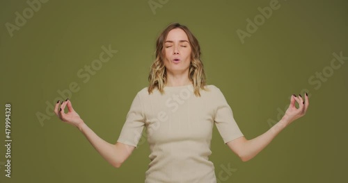 Young woman calming, breathing deep, meditating with mudra om gesture by hands, doing yogs exercise on green background