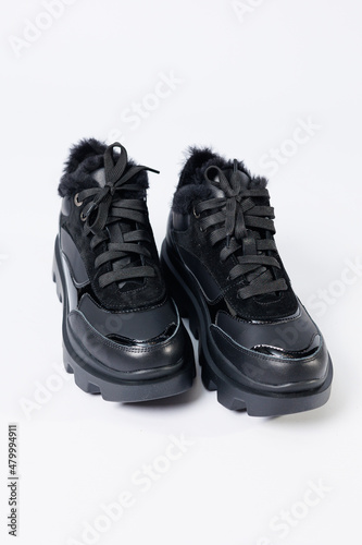 Women's fashionable black leather sneakers with fur on a white background. New collection of women's winter sneakers 2022