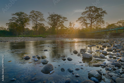 Beautiful sunrise over Murti river, riverbed in foreground with flowing water and stones. Scenic beauty of Dooars landscape, West Bengal, India photo