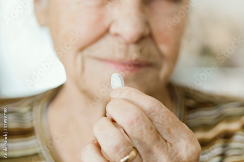 Title Close-up of elderly woman holding paxlovid pill before taking it.Selective focus on pill between fingers, woman looking at medication out of focus in background photo