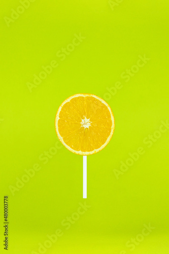 Orange lollipop with stick on light green background. Candy food minimal summer concept