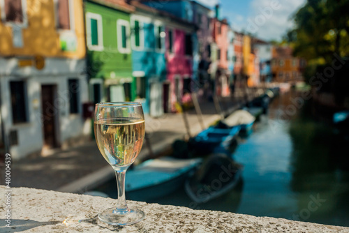 Wine glass of lonely tourist on small bridge in Venice at daytime. Water canals and embankments with bars and historical mansions of famous italian city