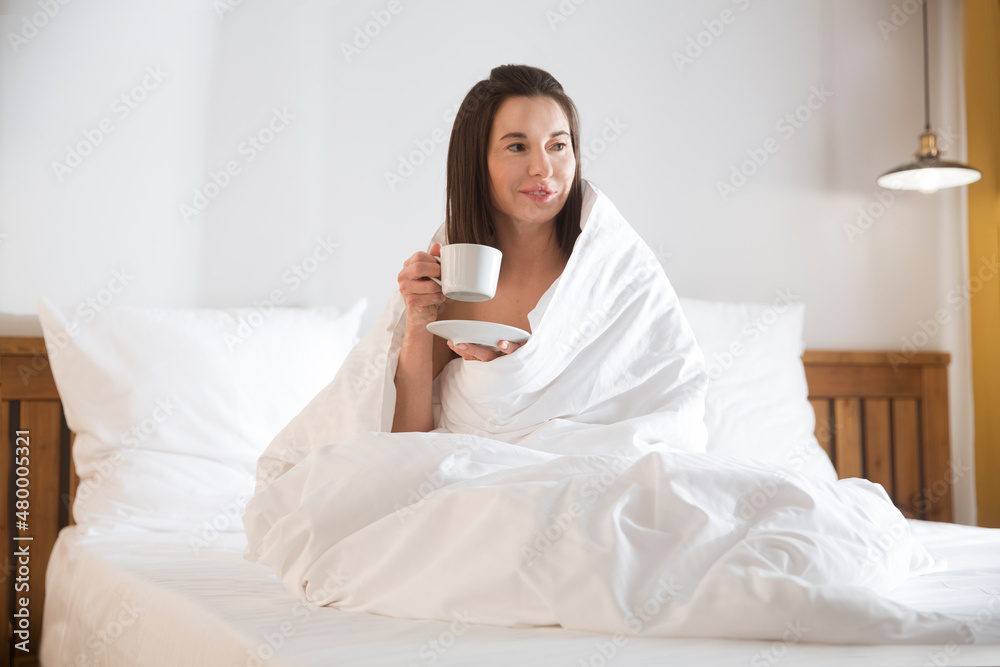 woman in a blanket drinks tea sitting in bed. enjoy the little things morning. slow life. woman in a blanket drinks tea sitting in bed. enjoy the little things morning. slow life.