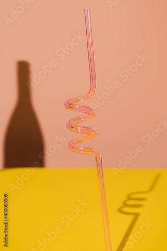 Pink cocktail straw and a shadow of a bottle on yellow background. Creative concept of party celebration design. Minimal abstract colourful and vivid wallpaper idea. photo