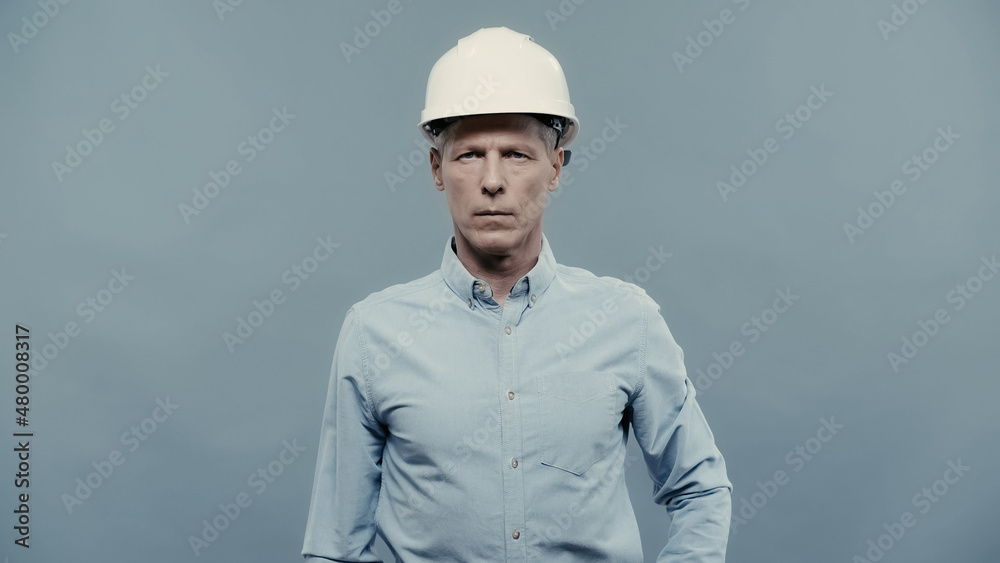 Mature engineer in protective helmet looking at camera isolated on grey. Mature engineer in protective helmet looking at camera isolated on grey.