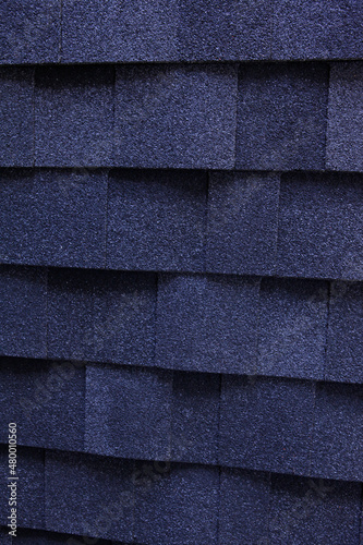 A dark blue architectural asphalt roofing shingles background. A close-up of a dimensional asphalt roofing shingles.