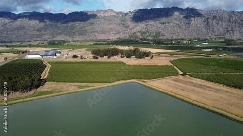  Big farm dam in a fertle valley with many fruit tree orchards on a cloudy morning with mountian in background camera slowly rising up showing faint clouds reflecting on water photo