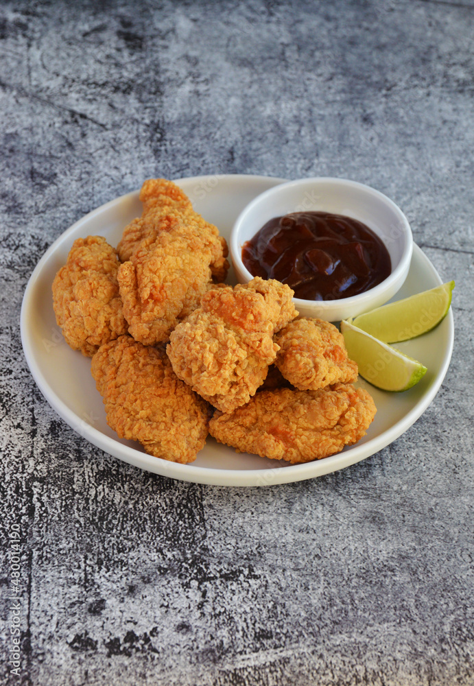 Crispy fried chicken served with BBQ sauce and lime wedges on the side in rustic background Crispy fried chicken served with BBQ sauce and lime wedges on the side in rustic background