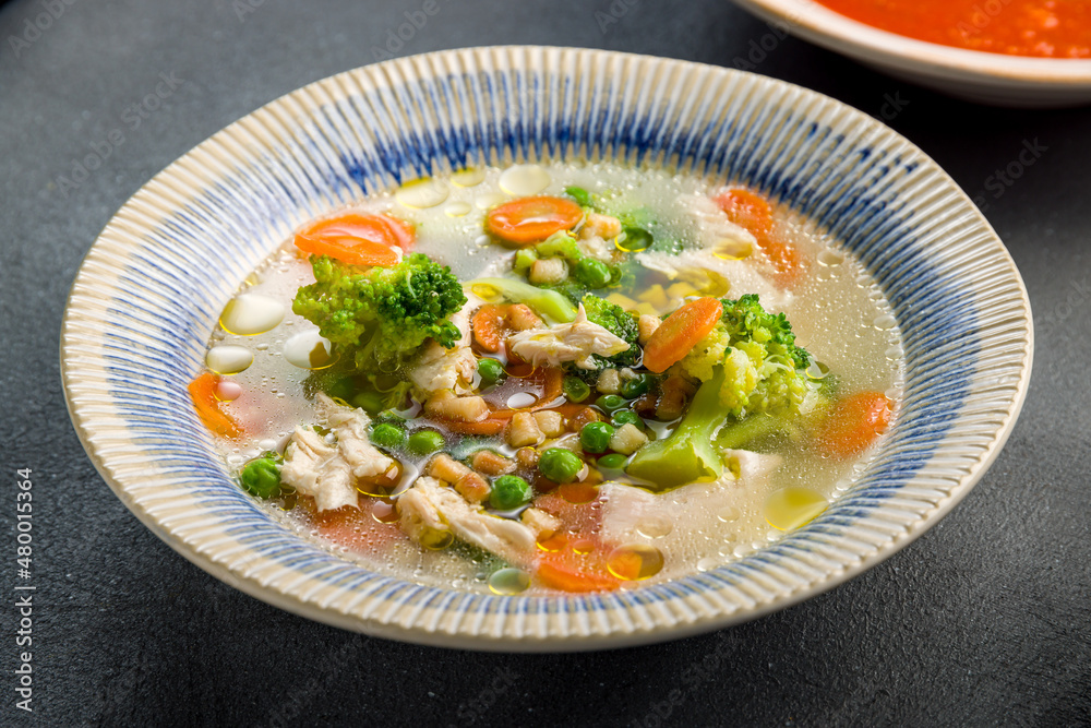 Chicken soup bouillon in a plate with vegetables on grey concrete table macro close up Chicken soup bouillon in a plate with vegetables on grey concrete table macro close up