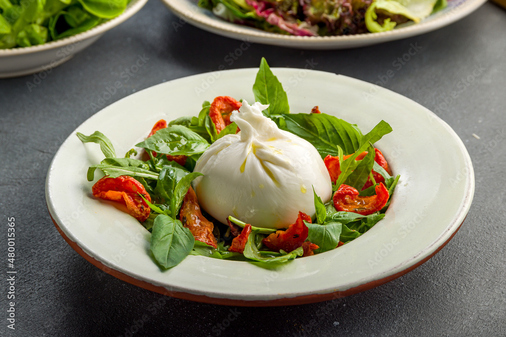Salad with buratta cheese, sun dried tomatoes and greens on grey concrete table Salad with buratta cheese, sun dried tomatoes and greens on grey concrete table
