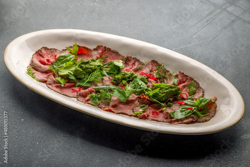 Sliced roast beef with greens and chili peppers on plate on grey concrete table