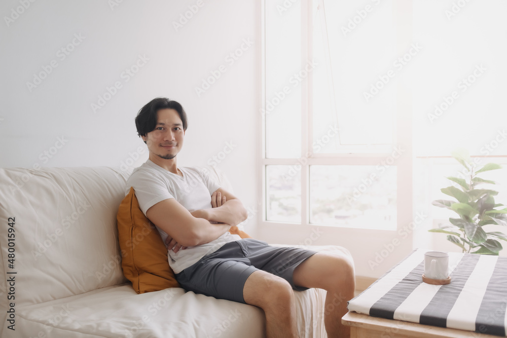Happy Asian man sits and relax on the sofa in the living room of the apartment. Happy Asian man sits and relax on the sofa in the living room of the apartment.