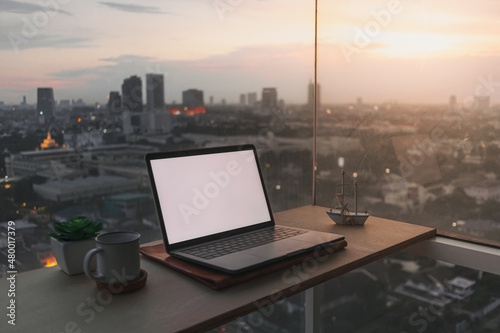 Laptop on wooden desk at the balcony with evening sunset city view.
