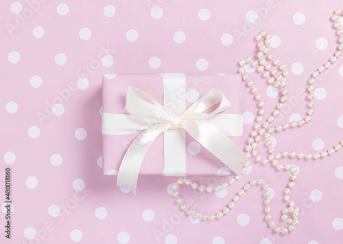 Pink polka dot gift box with pearl thread on pink background. Top view.